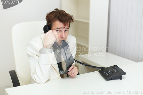 Image of Confused tousled man speaks on phone and chews tie