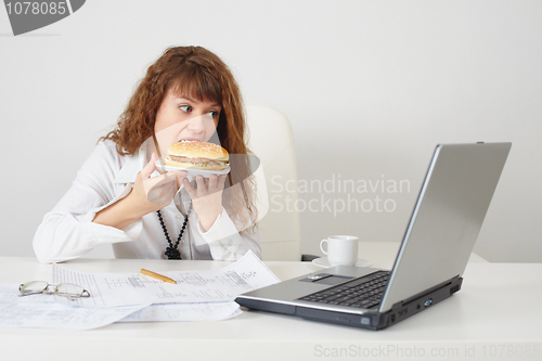 Image of Person at office on workplace eats a hamburger
