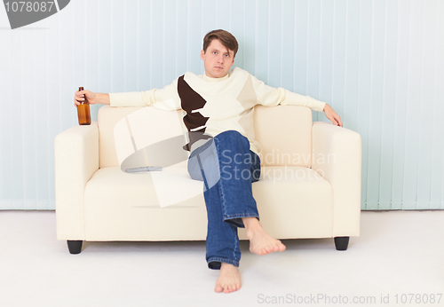 Image of Man sits on sofa with beer bottle in a hand