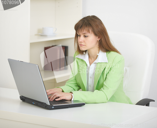 Image of Young woman sits at table at office with laptop