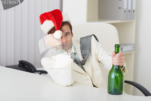 Image of Young man in christmas hat cap with bottle sits at table