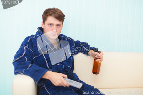 Image of Guy sits on sofa and drinks beer looking TV