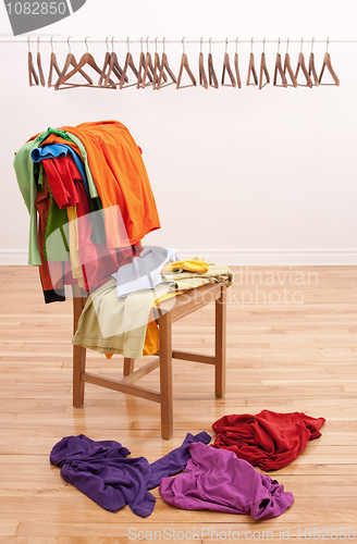 Image of Messy clothes on a chair and empty hangers on the background