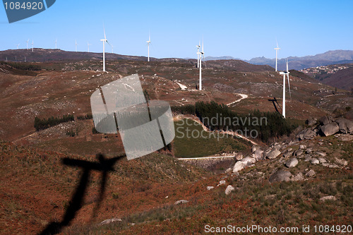 Image of mountain where the trees draw a heart with windmills power,  on blue sky;