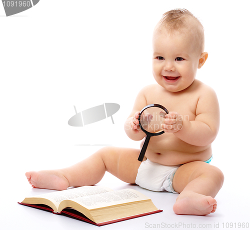 Image of Little child play with book and magnifier