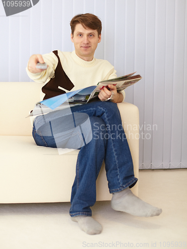 Image of Man sits on sofa with newspaper and remote control