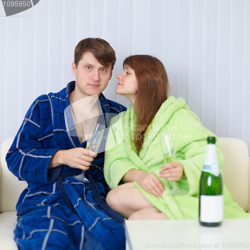 Image of Young people sit at home on sofa in dressing gowns with fizz