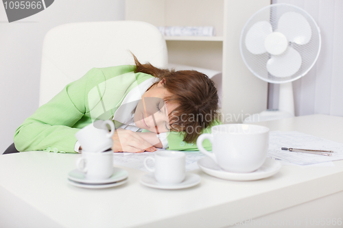 Image of Tired woman sleeping on desk in the office among coffee cups