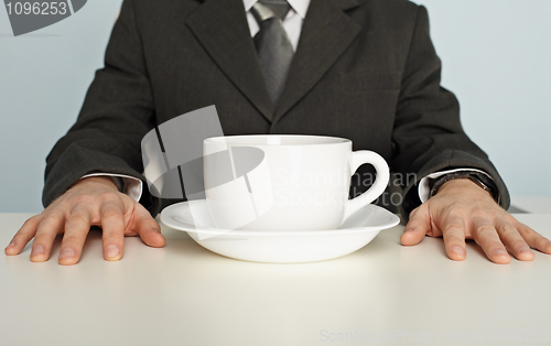 Image of Huge cup of coffee on table near businessman