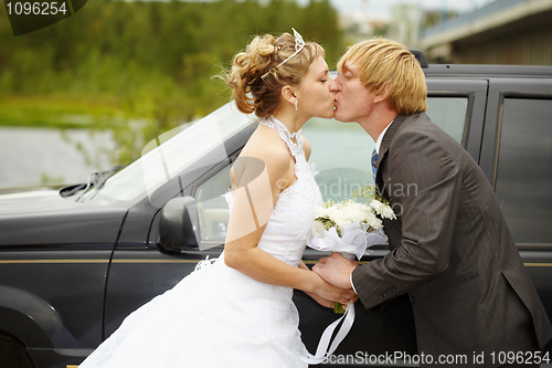 Image of Bride and groom kissing near a car