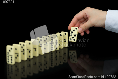 Image of Hand builds a line of dominoes on black background