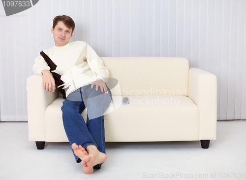 Image of Young man sits on sofa and has rest