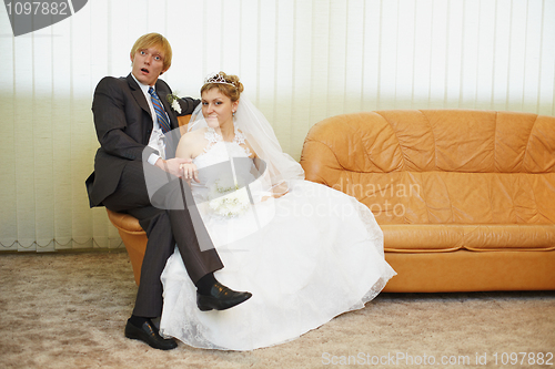 Image of Amusing groom and bride sitting on armchair