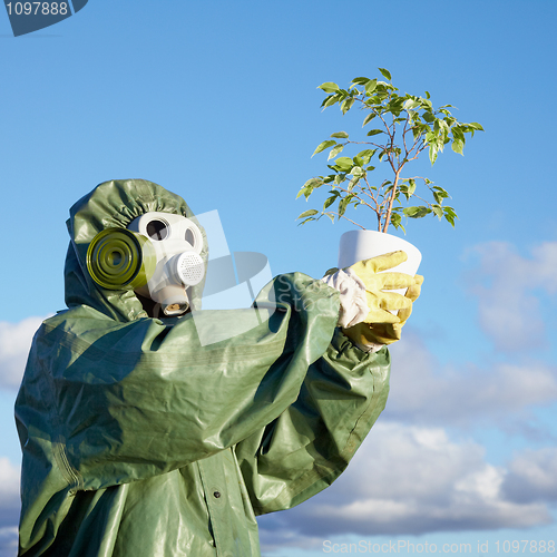 Image of Man in chemical suit and gas mask with plant in hands