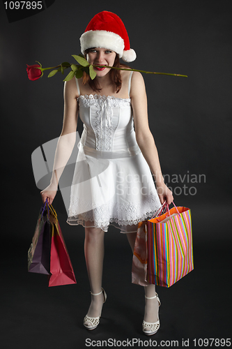 Image of Amusing girl in Christmas cap, with purchases and rose