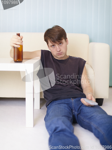 Image of Drunk man sits on floor at TV with a bottle