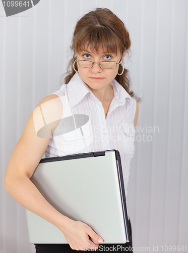 Image of Serious girl holds closed laptop in hand