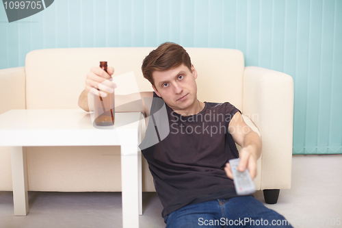 Image of Drunk guy with bottle of beer, TV changes channels