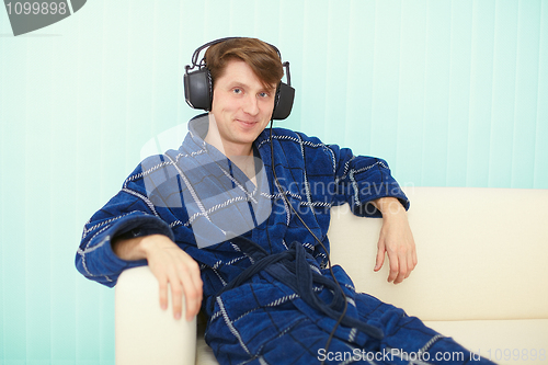 Image of Man in big ear-phones sits on sofa