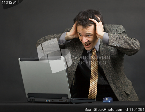 Image of Ðoung man shouts with despair looking at computer screen