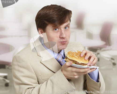 Image of Young funny businessman eats a hamburger
