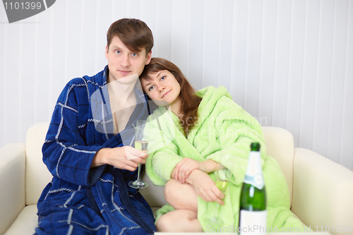 Image of Young couple in dressing gowns sitting on couch with fizz