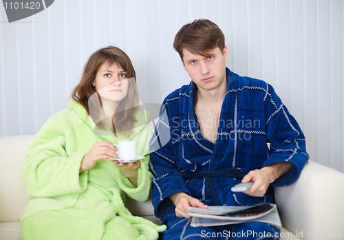 Image of Couple in dressing gowns sitting on couch and watching TV in dis