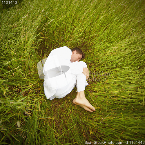 Image of Man lying on grass in fetal position