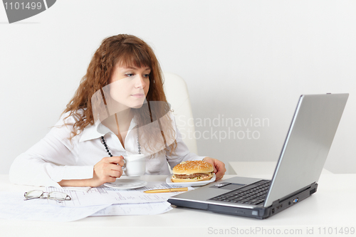 Image of Girl, on workplace is going to eat hamburger