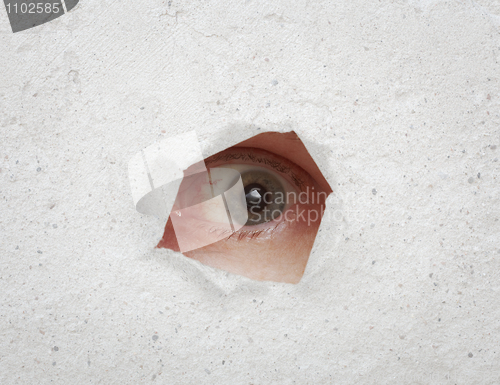 Image of Eye looking through hole in gray wall