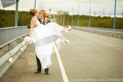 Image of Groom carries his bride in his arms on bridge