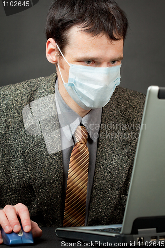 Image of Man in medical mask works with laptop