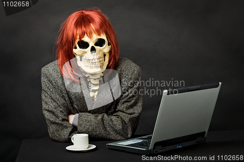 Image of Man dressed as death sits at table with computer