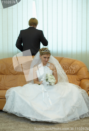 Image of Bride sitting on couch, groom looks out window