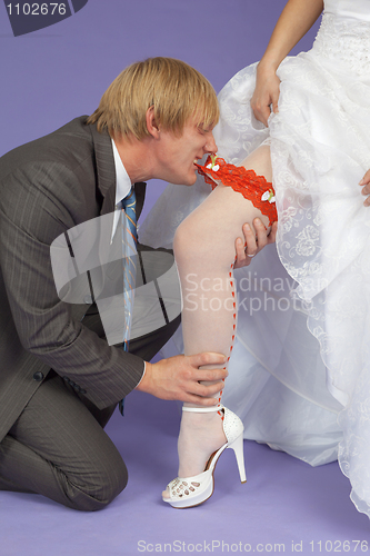 Image of Amusing groom removes a garter from leg of bride