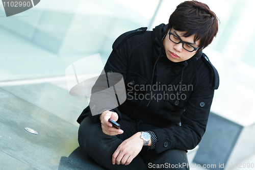 Image of casual asian man texting on cell phone