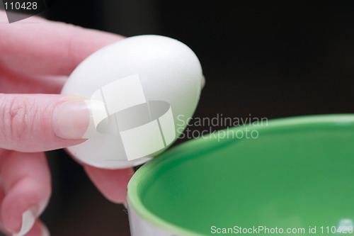 Image of Hand holding an egg over green bowl