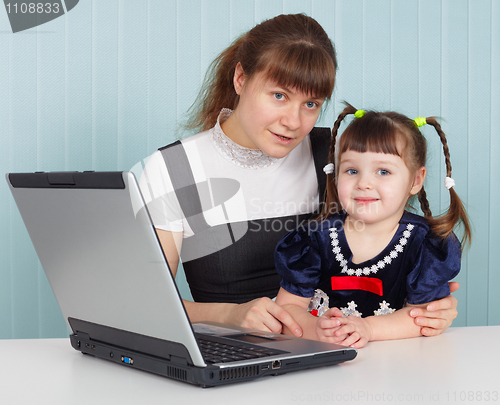 Image of Mother and daughter sitting at table with computer