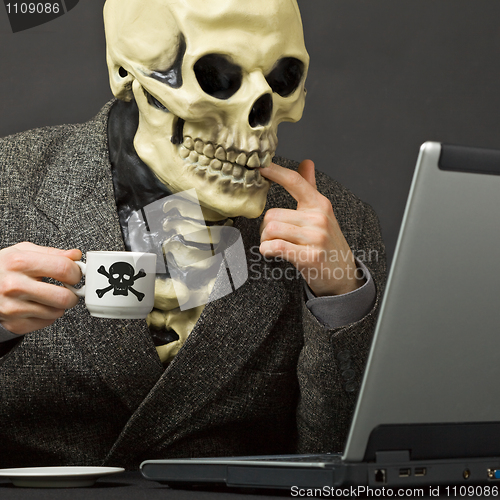 Image of Skeleton drinks poisonous coffee at table with laptop