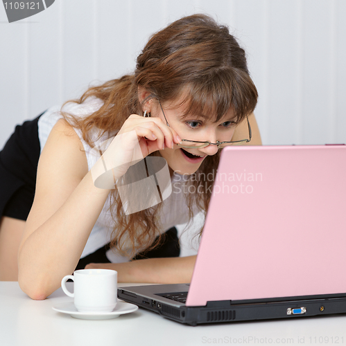 Image of Young woman working with pink  laptop computer at table