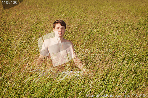 Image of Man sits in grass in lotus pose