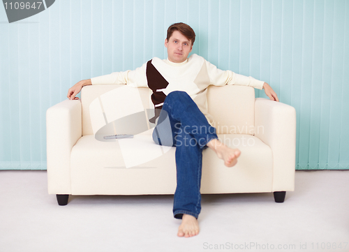 Image of Young man sits comfortably on soft sofa