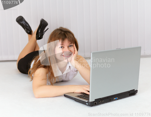 Image of Happy young woman lying on floor with laptop