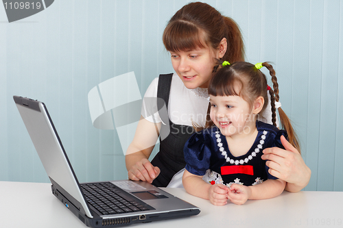 Image of Mother and daughter sitting at table with laptop