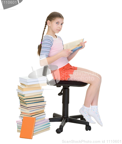 Image of Schoolgirl learns lessons near big pile of textbooks