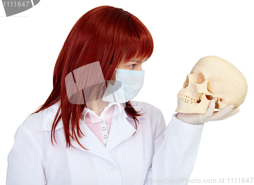 Image of Woman in medical uniform looks at human skull