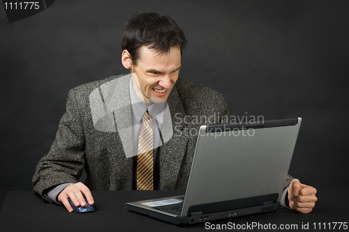 Image of Furious man sits at table and looks at laptop screen