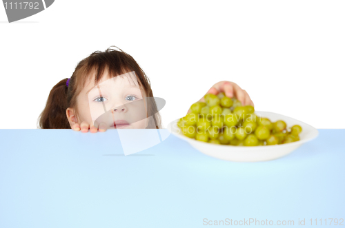 Image of Child reaches for grapes lying on table