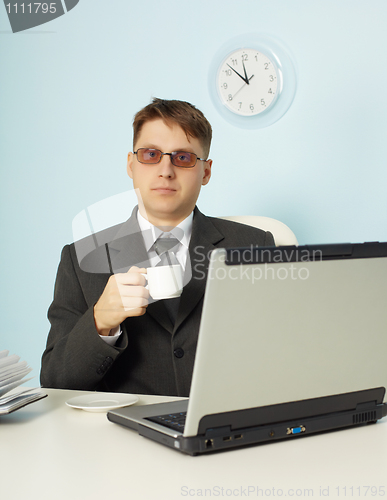 Image of Serious man at office with laptop and cup of coffee