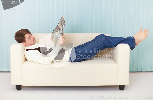 Image of Young woman lies comfortably on sofa with a magazine